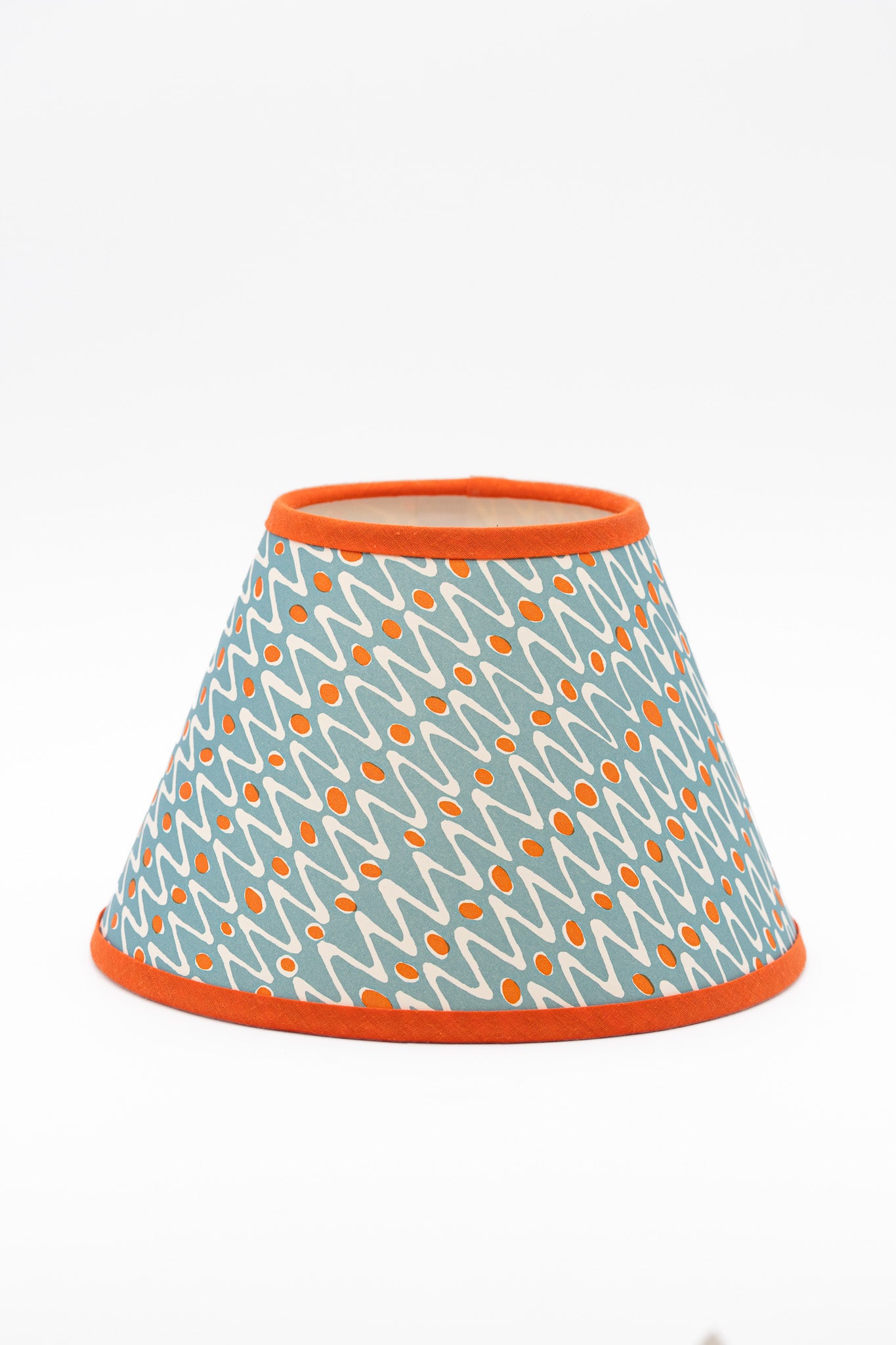A conical lampshade with a light blue, orange and white geometric pattern and orange trim on the top and bottom edges, shown against a plain white background.