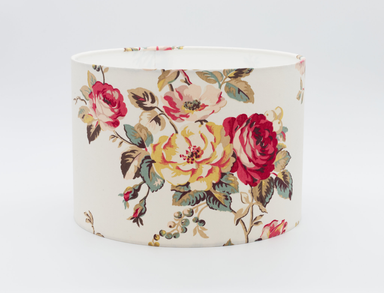 A drum lampshade in a big floral pattern of roses and leaves. Set on a white background.