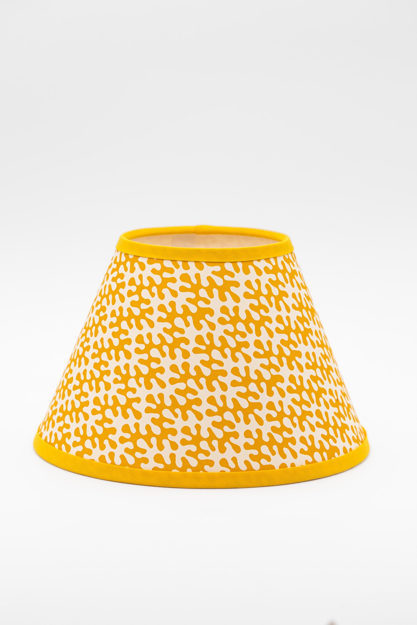 A paper lampshade with a yellow and white abstract pattern, featuring solid yellow trim at the top rim, bottom edge, and side flange, shown against a plain white background.