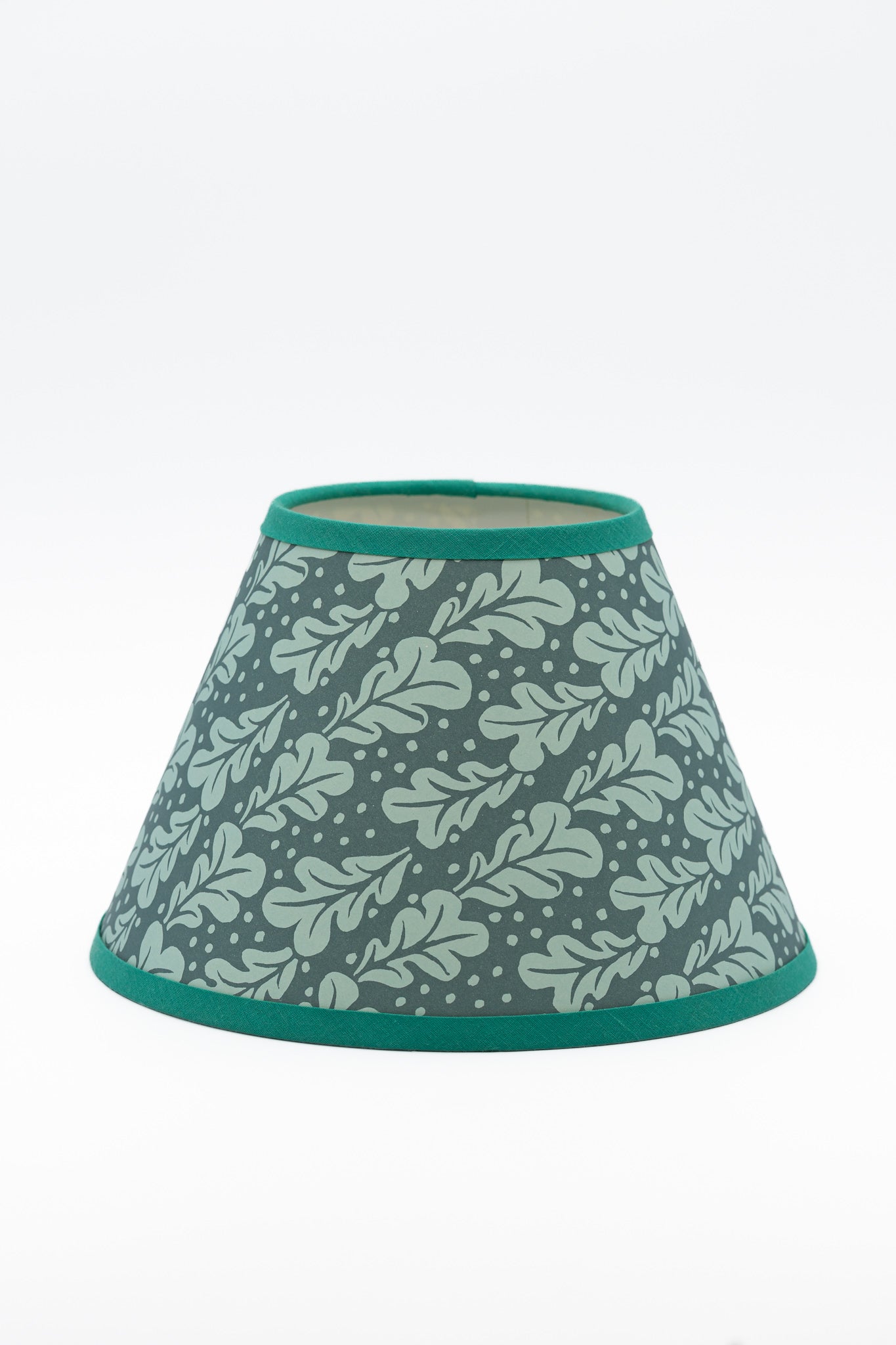 A paper lampshade with a duck egg blue  and teal pattern of leaves and small dots, finished with solid teal trim at the top and bottom.