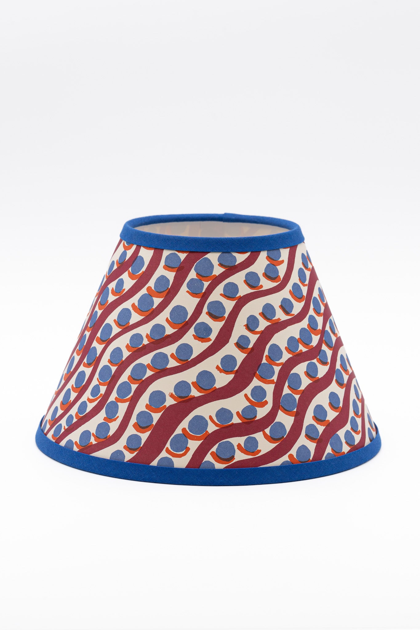 A paper lampshade featuring a wavy red and orange pattern with blue polka dots on a white background, finished with a solid blue trim.