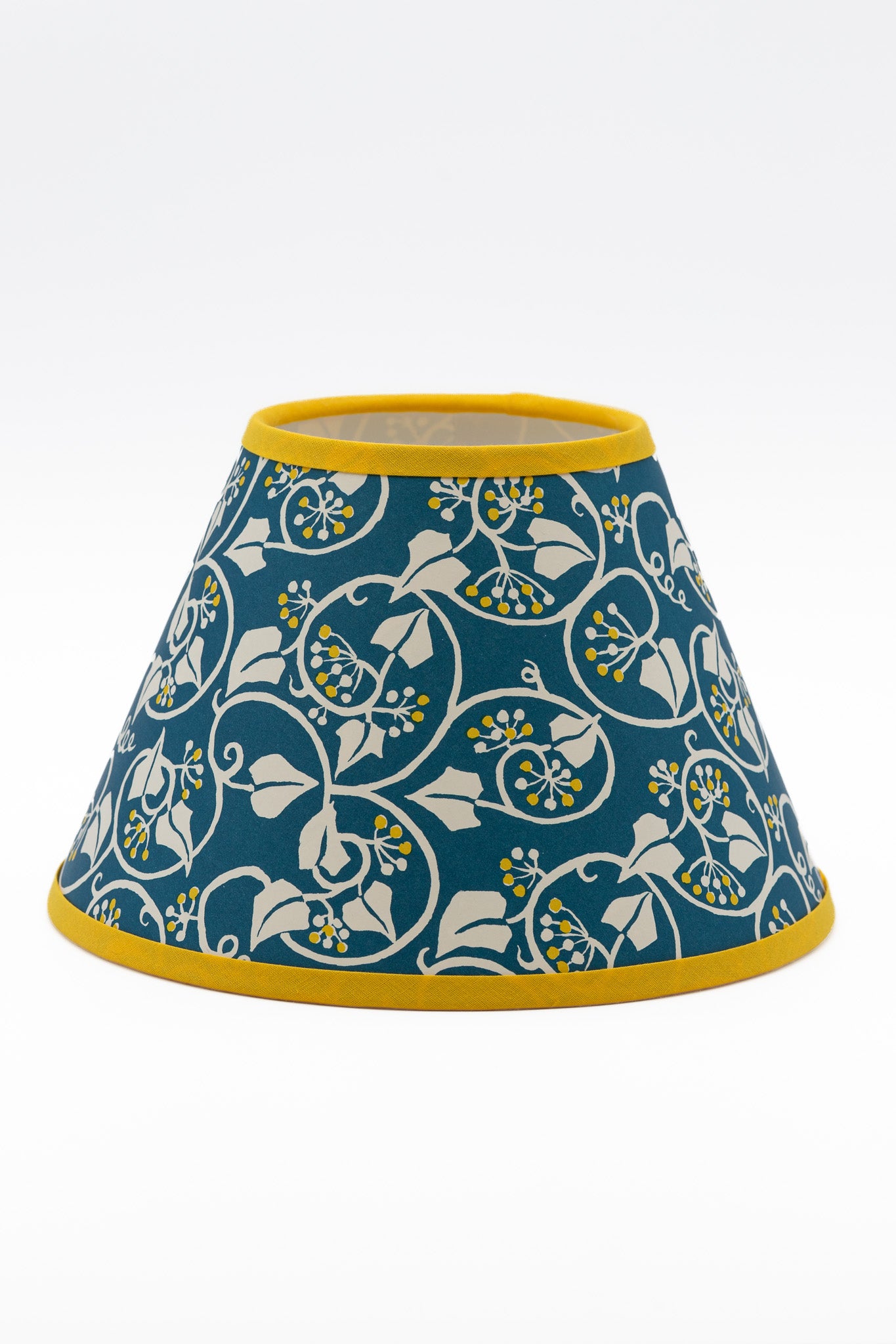 A paper lampshade featuring a teal blue background with a white floral and vine pattern, accented with yellow trim at the top rim, bottom rim, and center details.