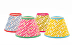 Four fabric lamp shades with colorful wavy dot patterns, arranged in a row against a plain white background. The shades feature different color combinations: blue-gray, pink, mustard yellow, and bright yellow, each with contrasting trim at the top and bottom.
